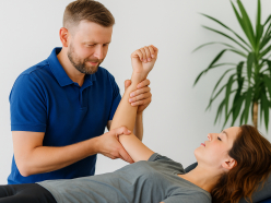 Therapeut in blauem Shirt behandelt liegende Patientin und hält ihren Arm fest